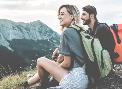 Wanderer schauen von einem Berggipfel herab in die Landschaft.