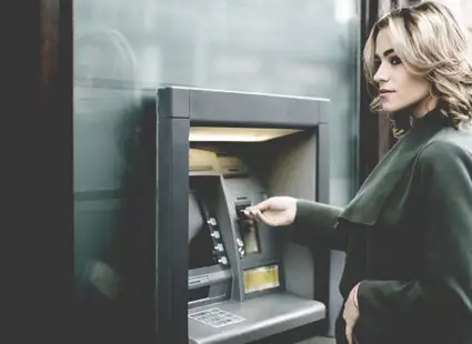 Studentin steht vor Bankautomat und holt Bargeld ab.