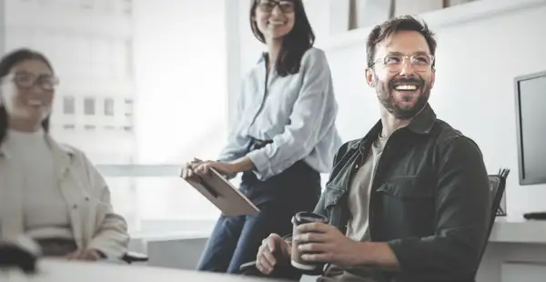 Ein Wirtschaftspsychologe sitzt mit Kolleg*innen im Büro und unterhält sich mit ihnen.