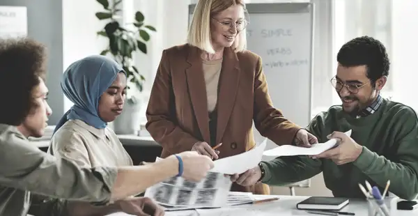 Eine Soziologie-Professorin arbeitet mit einer Gruppe von Studierenden an einem Projekt. Sie verteilt Dokumente und diskutiert die Inhalte mit ihnen.