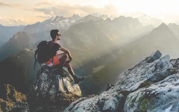 Ein Wanderer sitzt auf einem Berg und schaut in die Ferne.