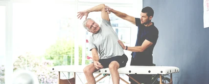 Junger Sporttherapeut behandelt einen älteren Patienten.
