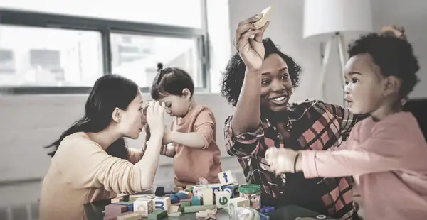 Zwei Frühpädagoginnen spielen mit zwei Kleinkindern. 