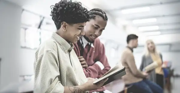 Personalmanagement Studenten stehen in der Uni-Bibliothek und schauen in ein Buch rein