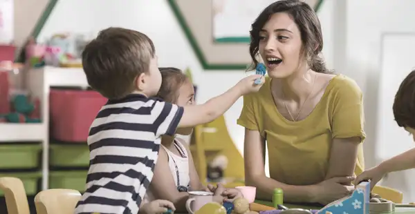 Eine duale Pädagogikstudentin interagiert spielerisch mit mehreren Kindern in einem Kindergarten.