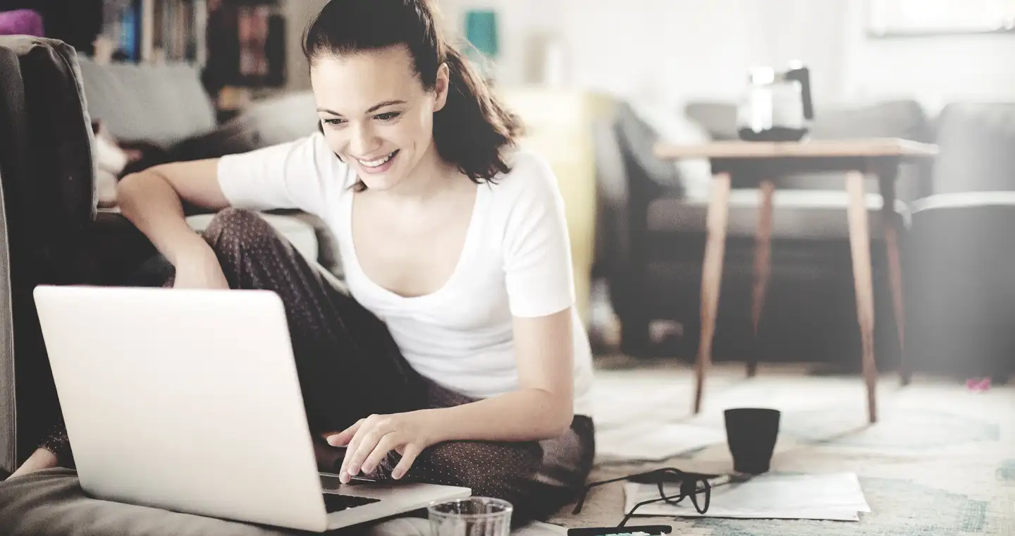 Eine junge Frau recherchiert auf dem Boden sitzend ein duales Studium Wirtschaftspsychologie am Laptop.