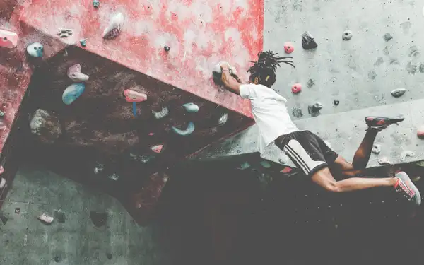 Ein sportlicher junger Mann in lässigen Sportklamotten lässt beim Bouldern an der Kletterwand seine Beine baumeln.