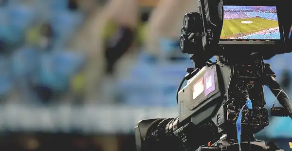 Eine professionelle Filmkamera filmt ein Fußballstadion.