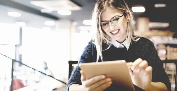 Junge, lächelnde Studentin lernt mit einem Tablet in der Hand.