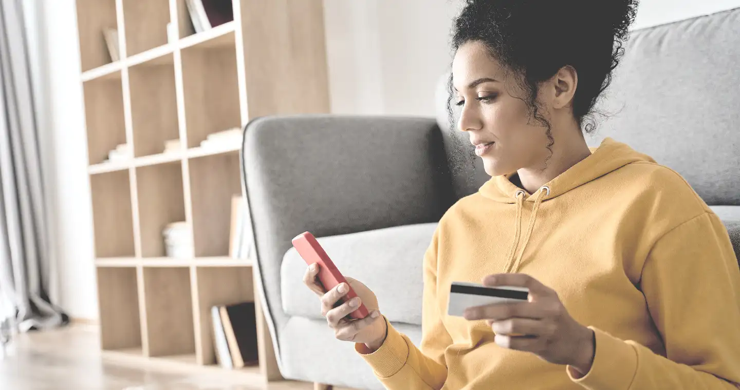 Eine junge Frau bezahlt etwas via Smartphone und Kreditkarte.