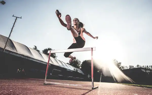 Eine junge Frau trainiert den Hürdenlauf auf der Laufbahn einer Sportanlage.