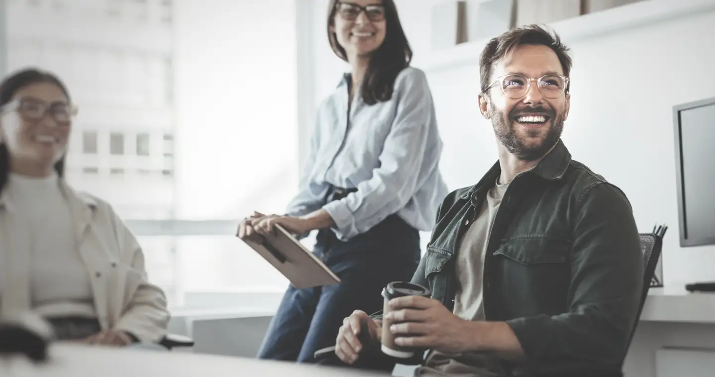 Ein Wirtschaftspsychologe sitzt mit Kolleg*innen im Büro und unterhält sich mit ihnen.