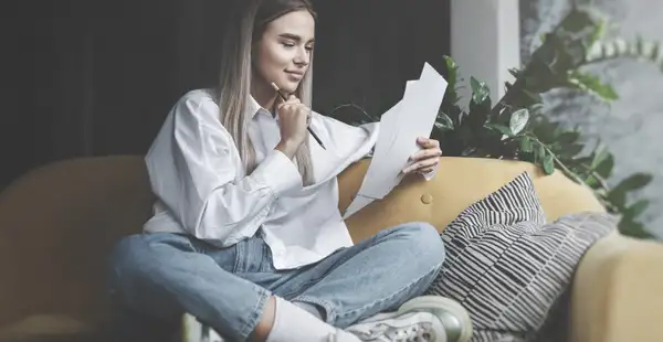 Eine Schulabsolventin sitzt auf der Couch und schreibt Stichpunkte für ein beispielhaftes Motivationsschreiben auf.