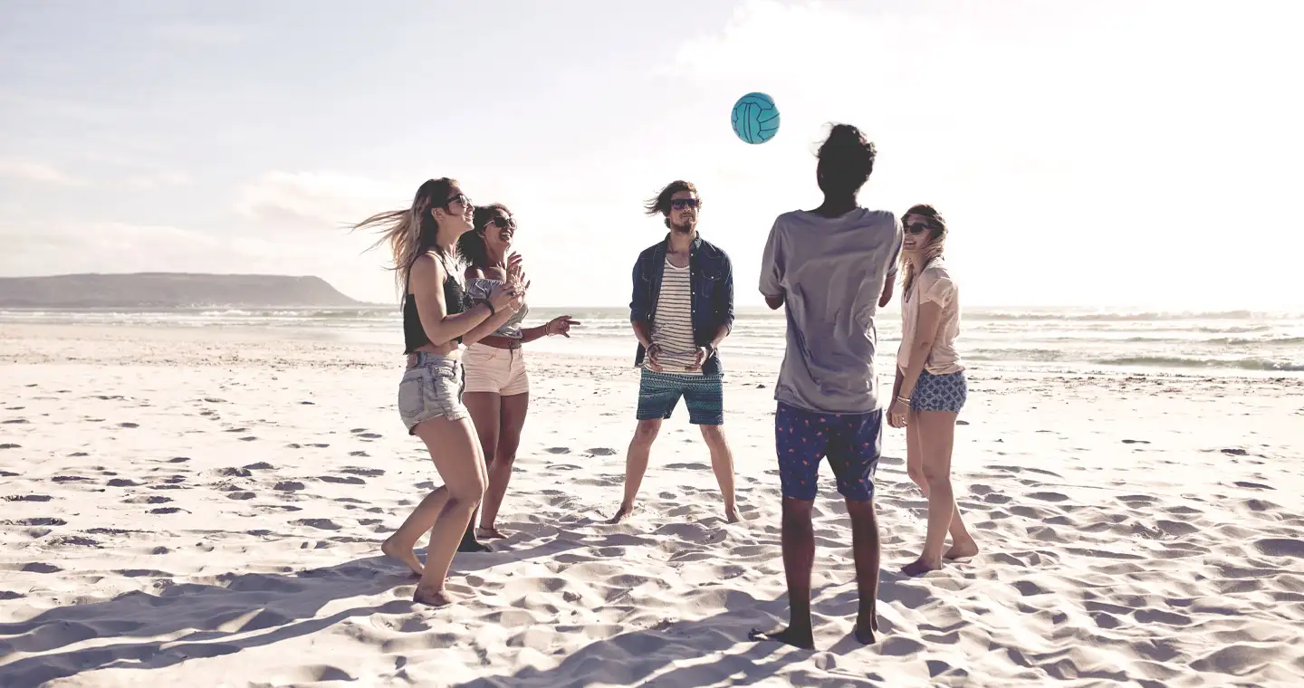 Studierende spielen Volleyball am Strand.