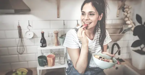 Eine junge Frau frühstückt lächelnd und überlegt, welchen Beruf sie im Ernährungsbereich ergreifen soll. 