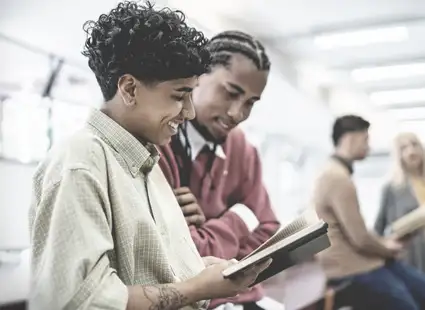 Personalmanagement Studenten stehen in der Uni-Bibliothek und schauen in ein Buch rein