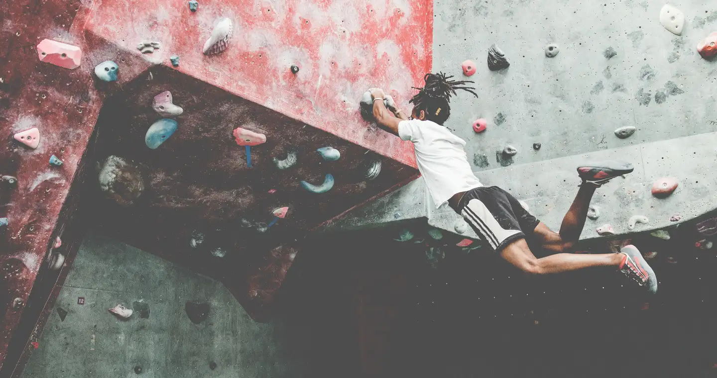 Ein junger sportlicher Mann bouldert eine Boulder-Wand hinauf.