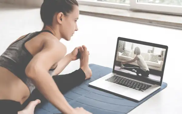 Eine junge Frau macht in ihrer Wohnung auf der Yogamatte Yoga vor ihrem Laptop