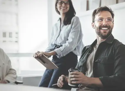 Ein Wirtschaftspsychologe sitzt mit Kolleg*innen im Büro und unterhält sich mit ihnen.