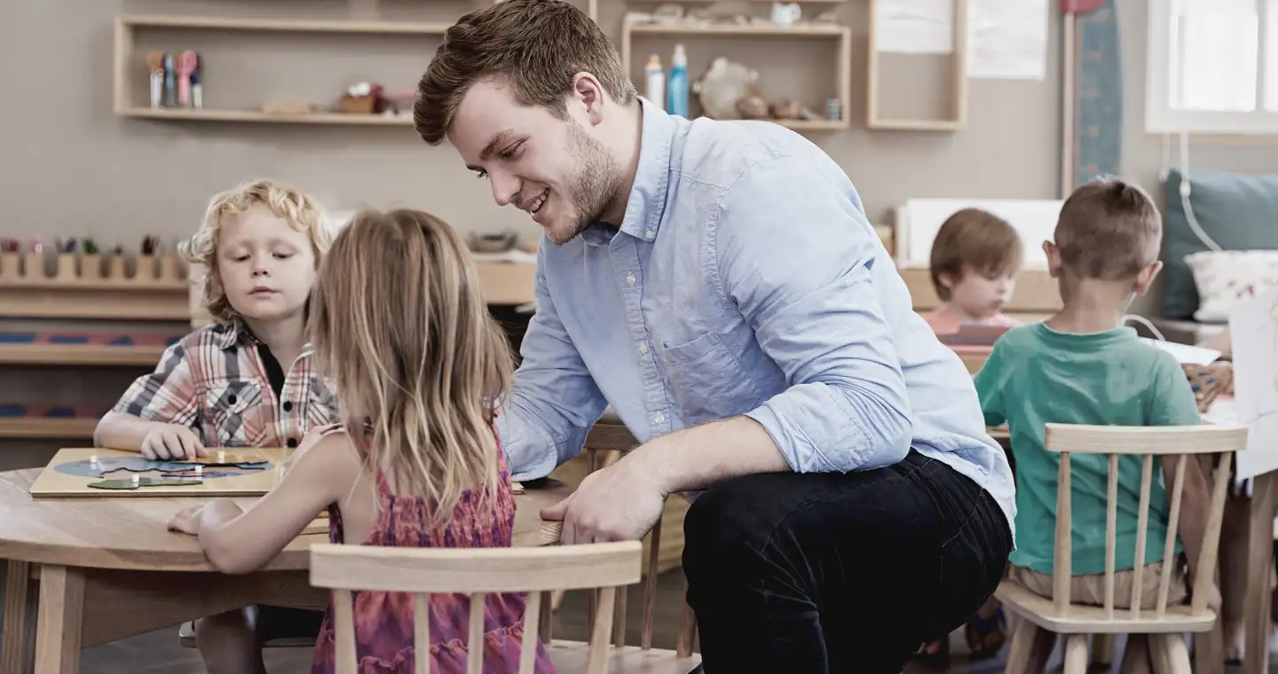 Ein Mann, der eine Weiterbildung im sozialen Bereich absolviert, arbeitet mit Kindern, die in einem Kindergarten sitzen.