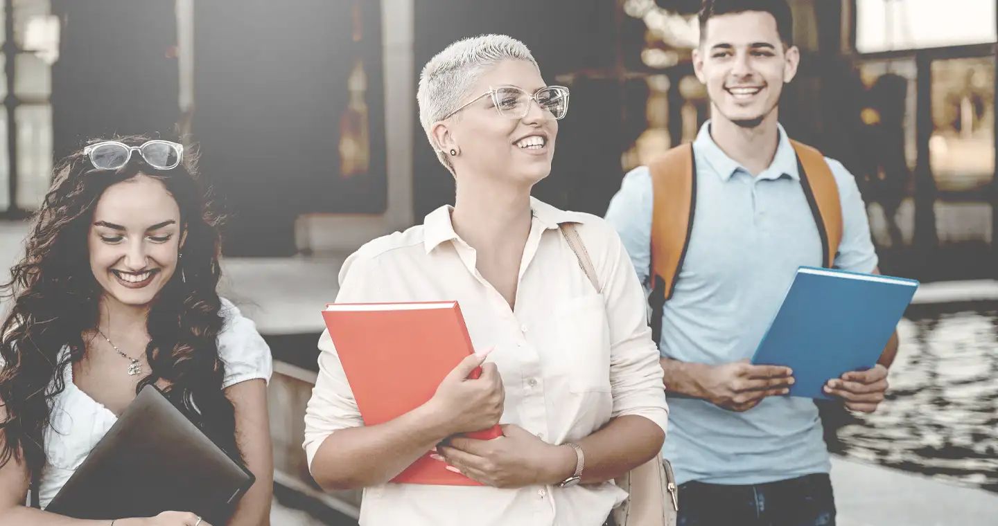 Eine Gruppe Studierender geht mit verschiedenfarbigen Notizmappen über den Campus. 