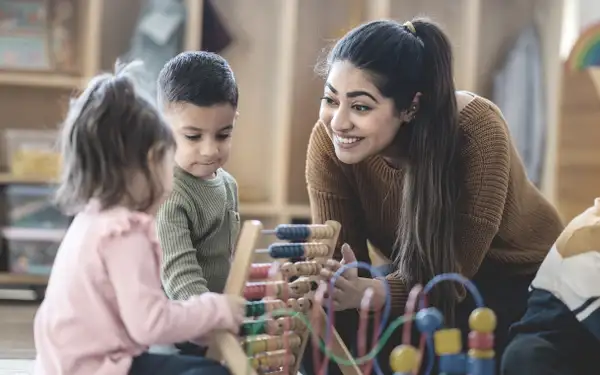 Eine Absolventin des Masterstudiengangs Pädagogik spielt mit Kleinkindern.