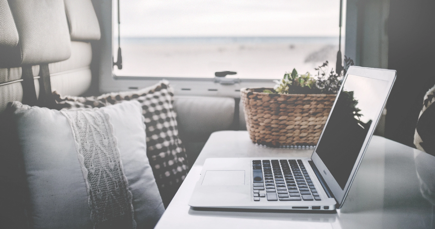 Ein Laptop steht auf dem Tisch in einem Ferienhaus am Strand. Dieses Bild soll die Option zum mobilen Arbeiten symbolisieren.