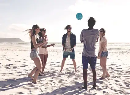 Junge Studierende spielen Volleyball am Strand.