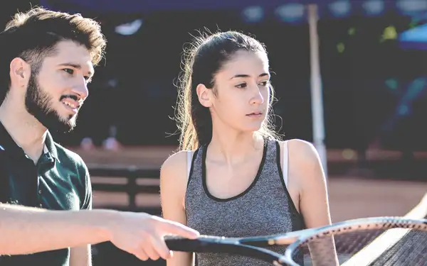 Spielerberater spricht mit junger Sportlerin auf einem Tennisplatz.