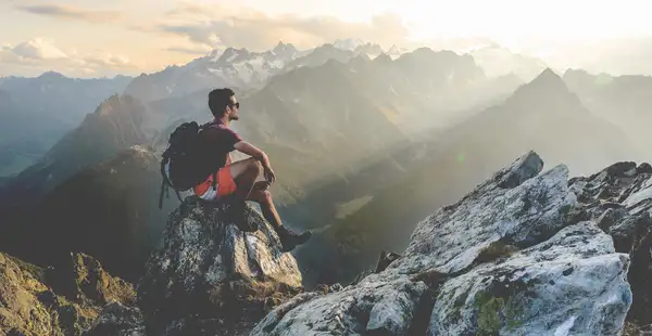 Ein Wanderer sitzt auf einem Berg und schaut in die Ferne.