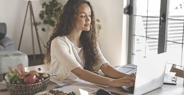 Eine junge Frau sitzt an einem Tisch und arbeitet an einem Laptop, während sie eine Ausbildung zur Ernährungsberaterin absolviert.