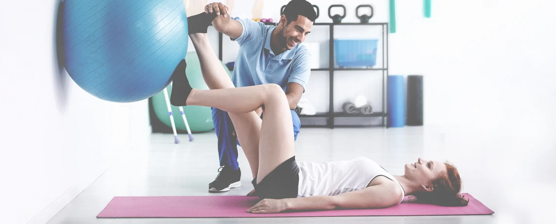 Ein Sporttherapeut leitet eine Patientin bei der Ausführung von Übungen mit einem Gymnastikball an.