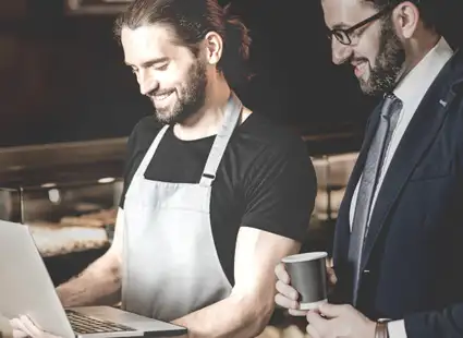 Zwei Personalmanager im Restaurant schauen gemeinsam in einen Laptop und lächeln.