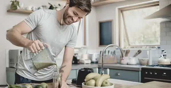 Ein Student des Studiengangs Sport und Ernährung bereitet in seiner modernen Küche einen grünen Smoothie zu.