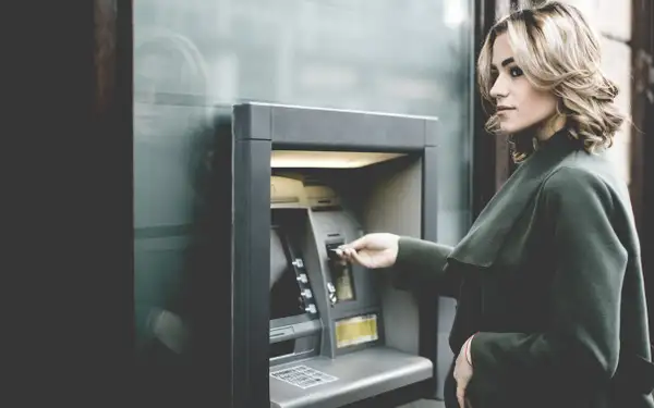 Studentin steht vor Bankautomat und holt Bargeld ab.