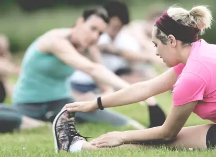 Sportstudierende machen Yoga auf einer Wiese.