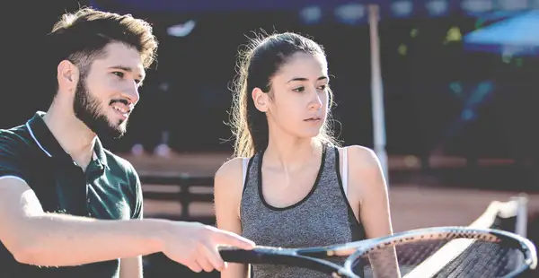 Spielerberater spricht mit junger Sportlerin auf einem Tennisplatz.