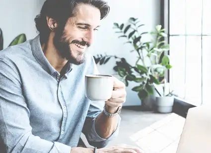 Junger Sportmanager sitzt in seinem Büro am Laptop und trinkt Kaffee.