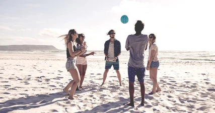 Junge Studierende spielen Volleyball am Strand.