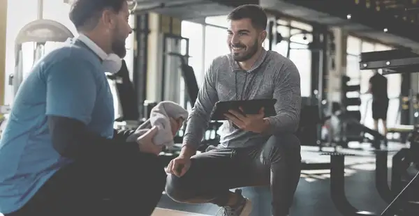 Ein Sportwissenschaftler berät einen Klienten im Fitnessstudio.