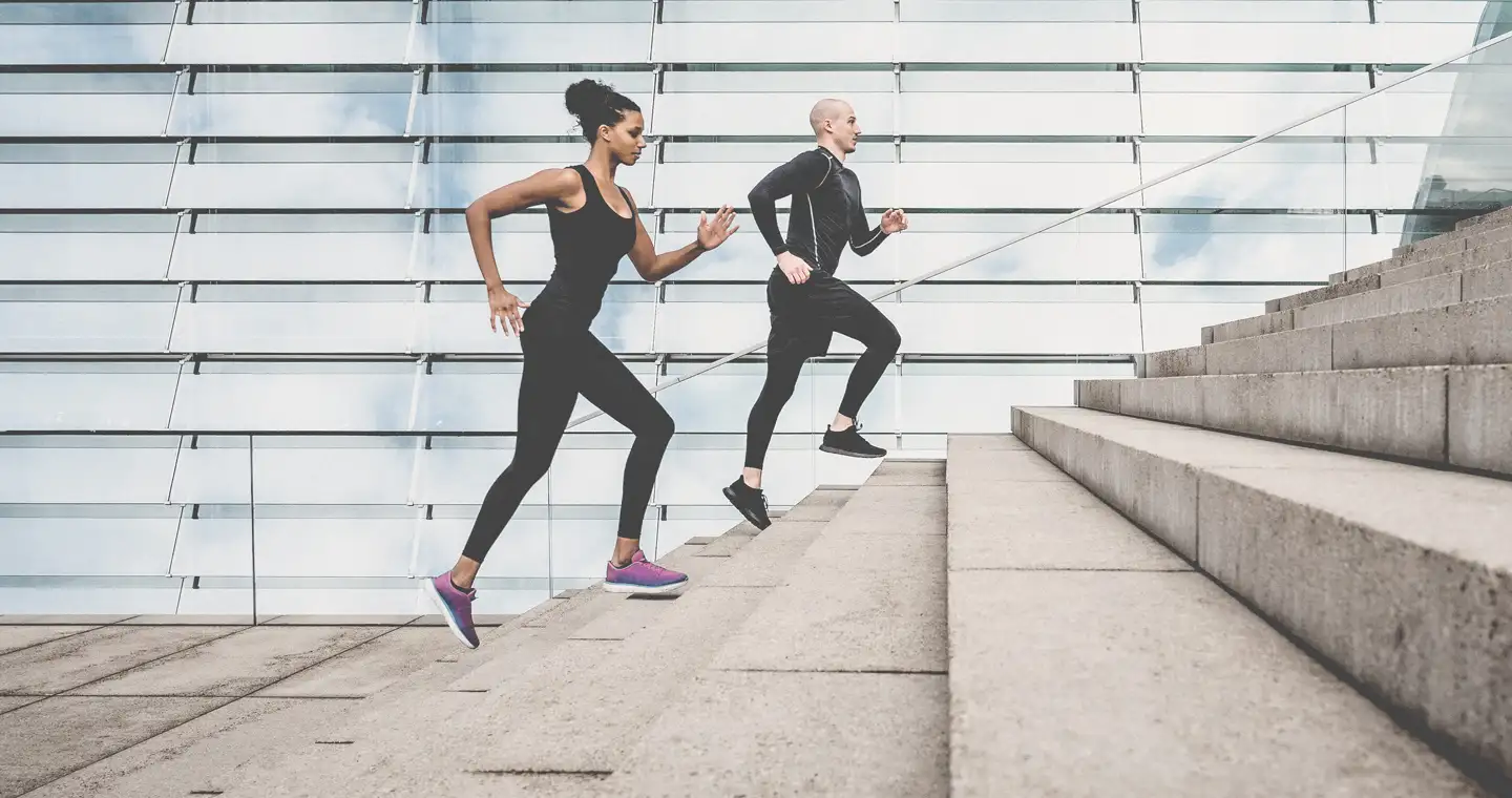 Eine Frau und ein Mann in Sportklamotten joggen eine Treppe hoch.