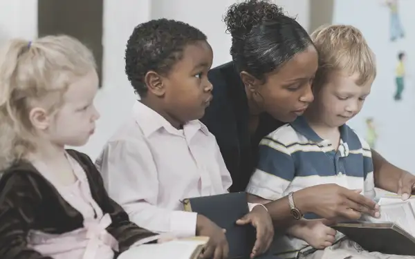 Eine Religionspädagogin liest einer Gruppe von Kindern aus der Bibel vor. Die Kinder hören aufmerksam zu.