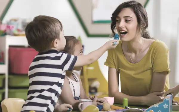 Eine duale Pädagogikstudentin interagiert spielerisch mit mehreren Kindern in einem Kindergarten.