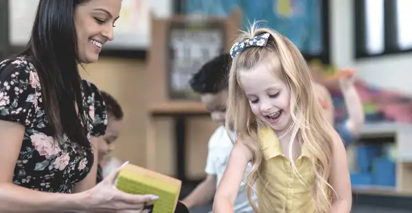 Eine duale Studentin, die Sozialpädagogik studiert, spielt fröhlich mit einem lächelnden Mädchen in einem Kindergarten.