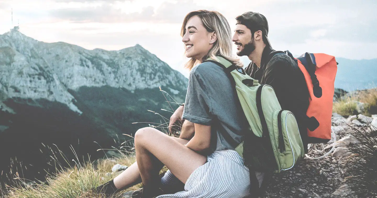 Sportlerin und Sportler sitzen auf einem Berggipfel nach einer Wanderung.