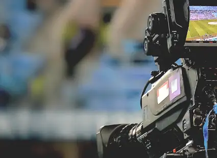 Eine professionelle Filmkamera filmt ein Fußballstadion.