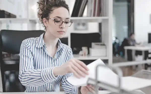 Eine Frau, die Bildungsmanagement studiert hat, arbeitet konzentriert in einem Büro und sortiert Dokumente.