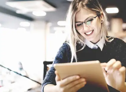 Junge, lächelnde Studentin lernt mit einem Tablet in der Hand.