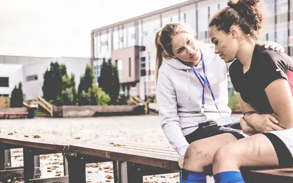Sportpsychologin berät eine junge Sportlerin. Sie sitzen gemeinsam draußen auf einer Bank.