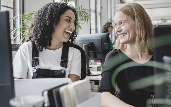 Zwei Masterstudentinnen im Studiengang Public Management arbeiten lächelnd in der Bibliothek an einem gemeinsamen Projekt.